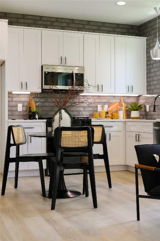 kitchen with decorative backsplash, white cabinets, decorative light fixtures, and light wood-type flooring