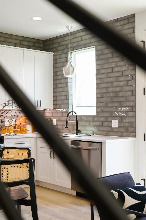 kitchen featuring pendant lighting, white cabinets, sink, light hardwood / wood-style flooring, and stainless steel dishwasher