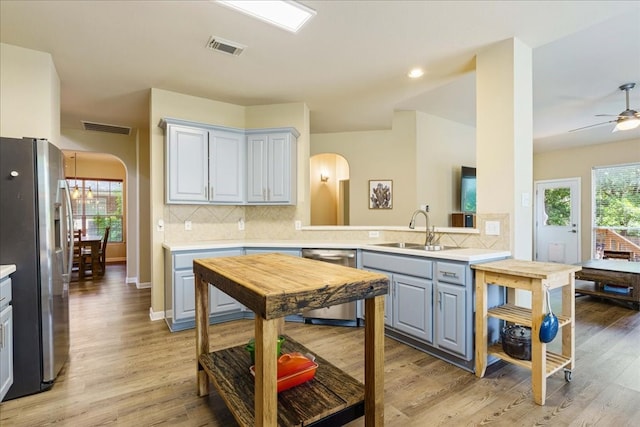 kitchen featuring sink, light wood-type flooring, backsplash, ceiling fan, and stainless steel appliances