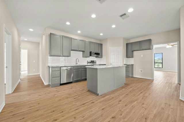 kitchen featuring a kitchen island, gray cabinetry, stainless steel appliances, light stone countertops, and light hardwood / wood-style floors