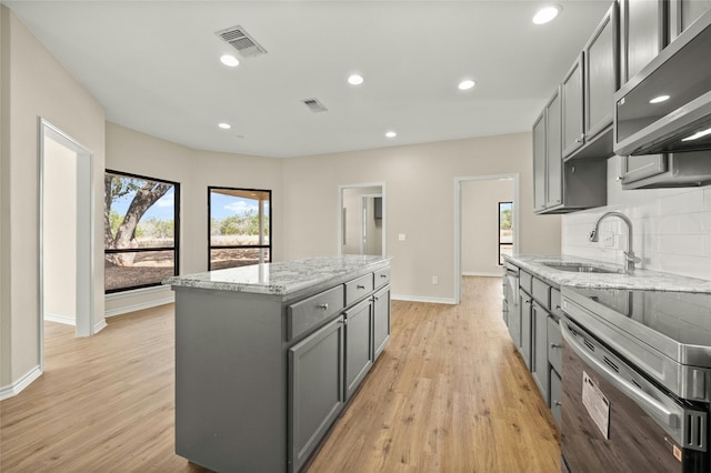 kitchen featuring light stone countertops, sink, a kitchen island, gray cabinets, and light hardwood / wood-style flooring