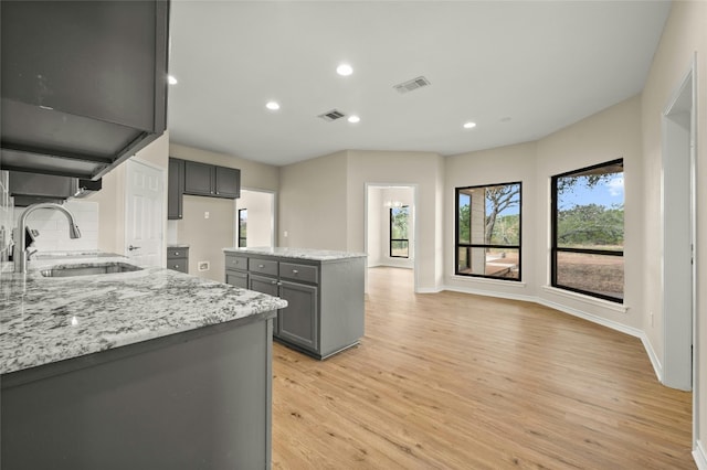 kitchen with light stone counters, sink, light wood-type flooring, and gray cabinetry