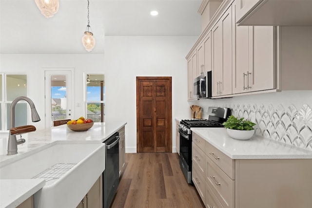 kitchen with appliances with stainless steel finishes, light stone counters, dark wood-type flooring, sink, and pendant lighting