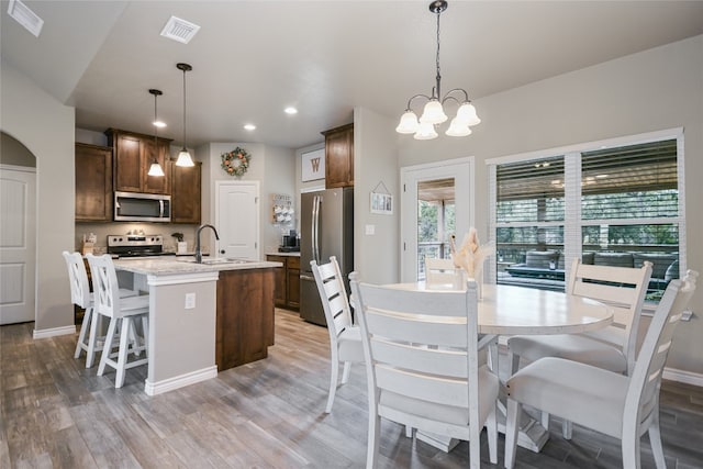 kitchen with appliances with stainless steel finishes, light hardwood / wood-style flooring, a center island with sink, and hanging light fixtures