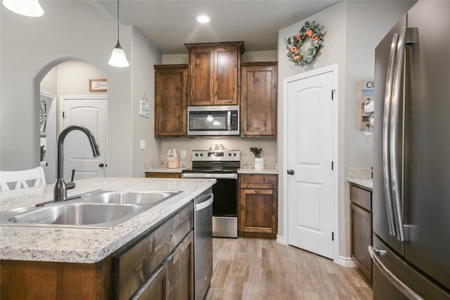 kitchen with a kitchen island with sink, sink, pendant lighting, light wood-type flooring, and appliances with stainless steel finishes