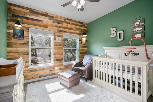 bedroom featuring a nursery area, wooden walls, and ceiling fan