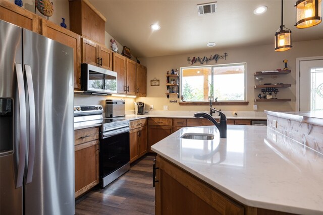 kitchen with dark wood-type flooring, an island with sink, hanging light fixtures, sink, and appliances with stainless steel finishes