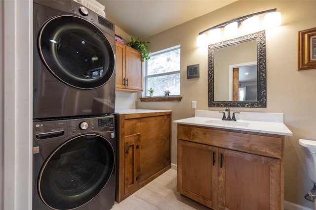 washroom with sink, stacked washer / drying machine, light hardwood / wood-style floors, and cabinets