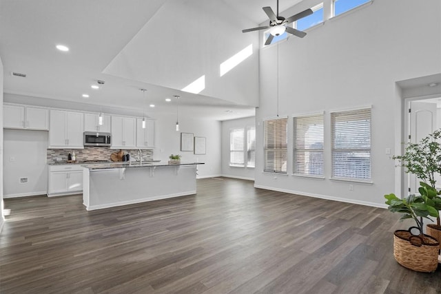 kitchen with pendant lighting, a breakfast bar, a center island with sink, decorative backsplash, and white cabinetry