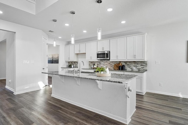 kitchen featuring white cabinetry, a center island with sink, light stone countertops, and decorative light fixtures