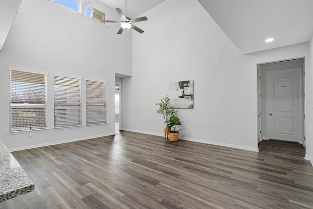 unfurnished living room with ceiling fan, a towering ceiling, and dark hardwood / wood-style floors