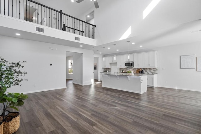 kitchen with white cabinetry, a high ceiling, backsplash, a kitchen island with sink, and a breakfast bar