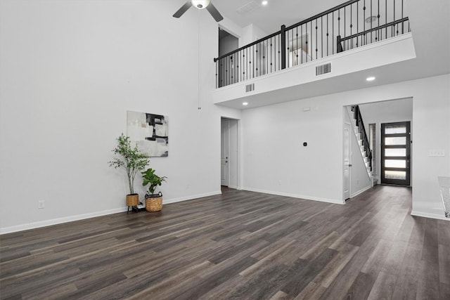 unfurnished living room with ceiling fan, dark hardwood / wood-style floors, and a high ceiling