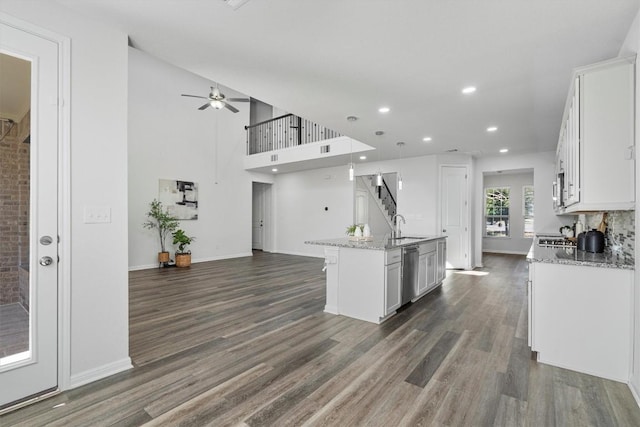 kitchen with white cabinetry, light stone countertops, dark hardwood / wood-style flooring, stainless steel dishwasher, and a kitchen island with sink