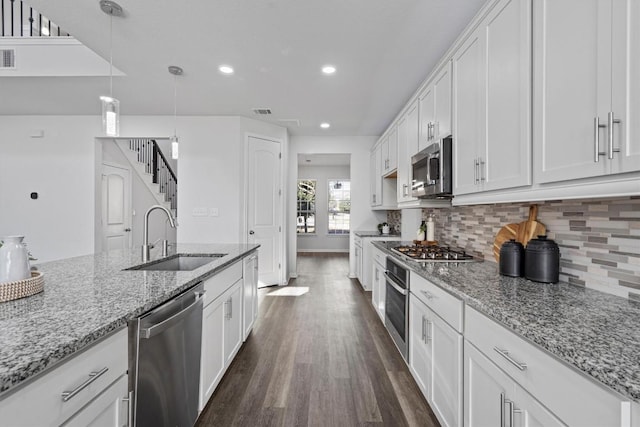 kitchen featuring white cabinets, sink, appliances with stainless steel finishes, decorative light fixtures, and light stone counters