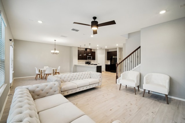 living room with light wood-type flooring, plenty of natural light, and ceiling fan with notable chandelier