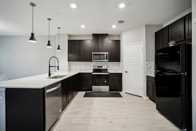 kitchen with kitchen peninsula, light wood-type flooring, stainless steel appliances, sink, and decorative light fixtures