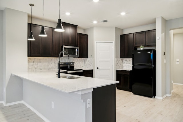 kitchen with kitchen peninsula, decorative backsplash, hanging light fixtures, appliances with stainless steel finishes, and light hardwood / wood-style floors