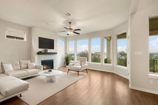 living room featuring dark wood finished floors, visible vents, a ceiling fan, a warm lit fireplace, and baseboards