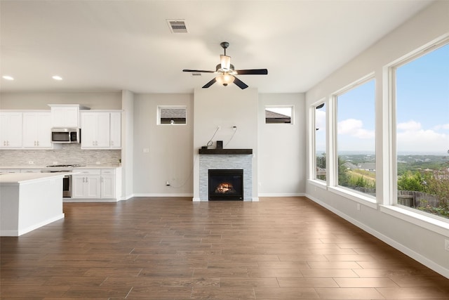 unfurnished living room with dark wood-type flooring, visible vents, a stone fireplace, and baseboards