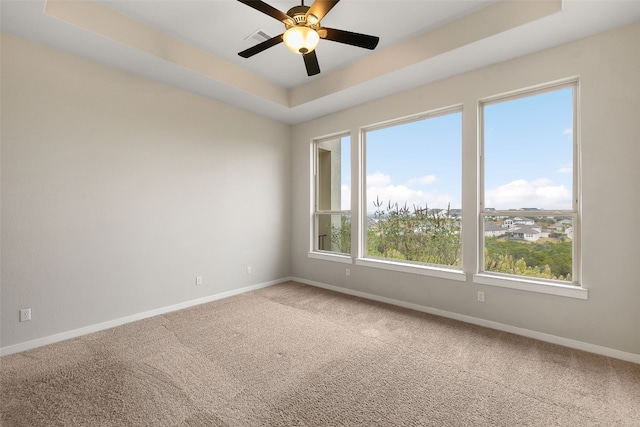 carpeted spare room with ceiling fan, a tray ceiling, visible vents, and baseboards