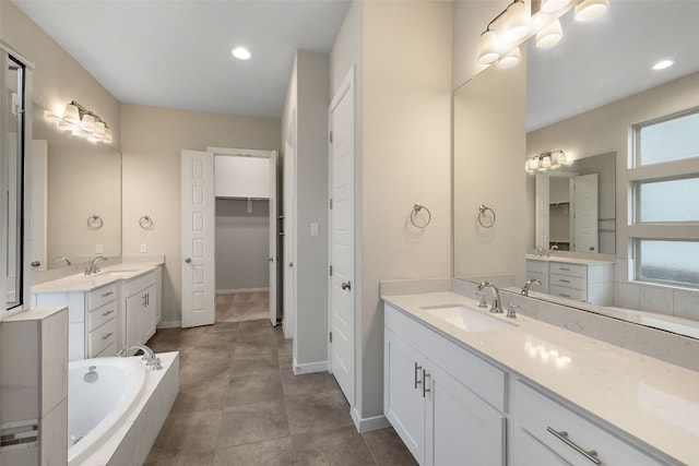 full bath with a walk in closet, a garden tub, two vanities, and a sink