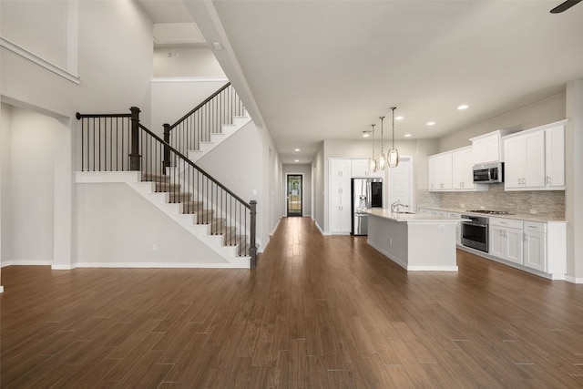 kitchen with dark wood-style flooring, stainless steel appliances, light countertops, a kitchen island with sink, and a sink