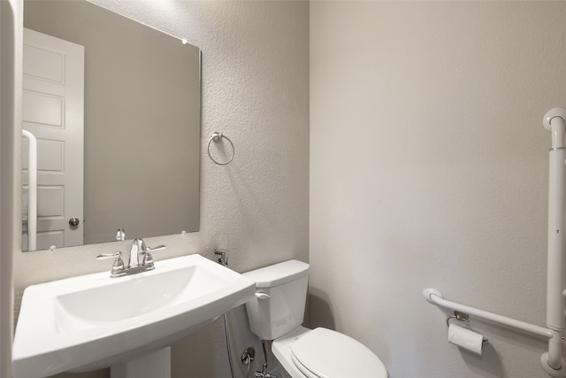 half bathroom featuring a textured wall, a sink, and toilet