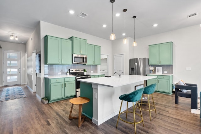 kitchen with a kitchen island with sink, a breakfast bar area, dark hardwood / wood-style floors, decorative light fixtures, and stainless steel appliances