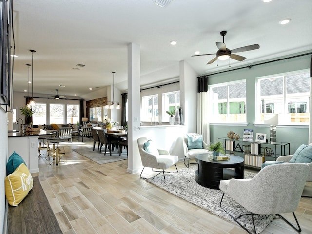 living room featuring light wood-type flooring, ceiling fan with notable chandelier, and sink