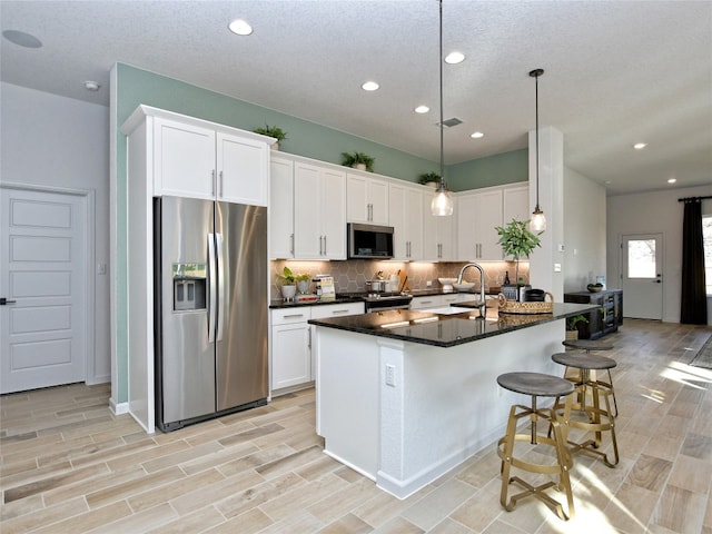 kitchen with stainless steel appliances, light hardwood / wood-style floors, a kitchen island with sink, white cabinets, and pendant lighting