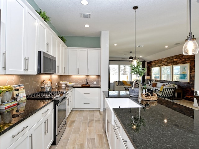 kitchen featuring dark stone counters, white cabinetry, hanging light fixtures, and stainless steel appliances