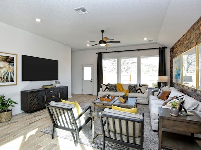 living room featuring ceiling fan, a textured ceiling, light wood-type flooring, and vaulted ceiling