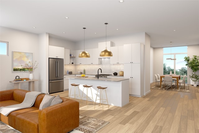 kitchen with stainless steel fridge, backsplash, pendant lighting, a center island with sink, and white cabinets