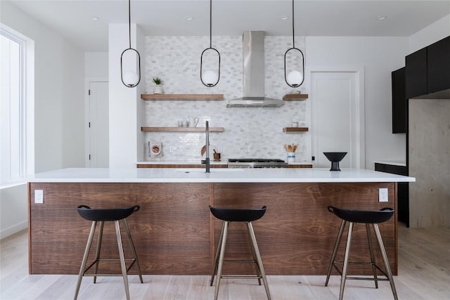 bar with pendant lighting, backsplash, wall chimney range hood, stainless steel stove, and light hardwood / wood-style floors