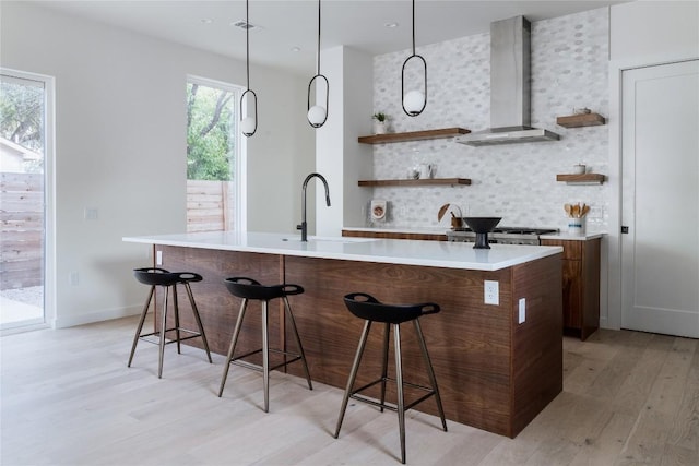 bar featuring decorative backsplash, wall chimney exhaust hood, sink, light hardwood / wood-style floors, and hanging light fixtures