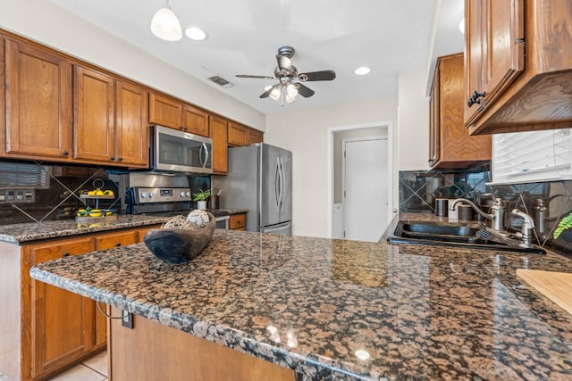 kitchen featuring sink, kitchen peninsula, appliances with stainless steel finishes, dark stone counters, and decorative backsplash