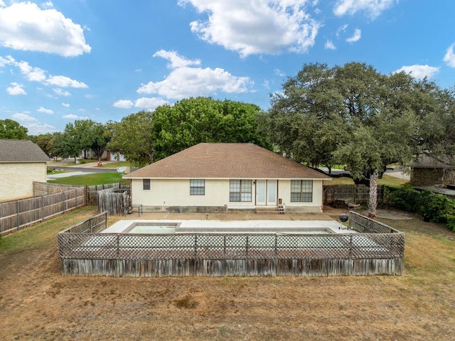 rear view of house with a hot tub, a patio, and a yard