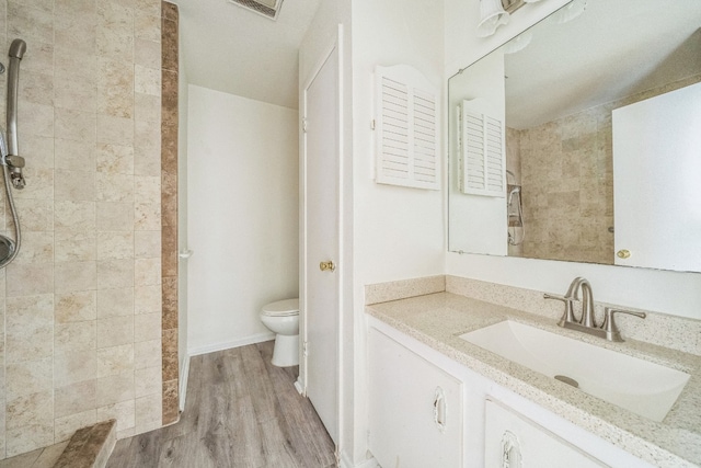 bathroom with toilet, vanity, wood-type flooring, and a tile shower