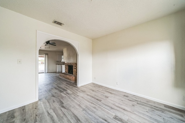 unfurnished room featuring a textured ceiling, light wood-type flooring, a fireplace, and ceiling fan