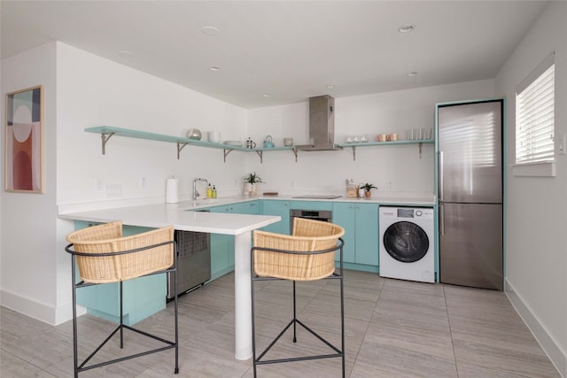 kitchen with kitchen peninsula, wall chimney exhaust hood, stainless steel appliances, washer / dryer, and sink