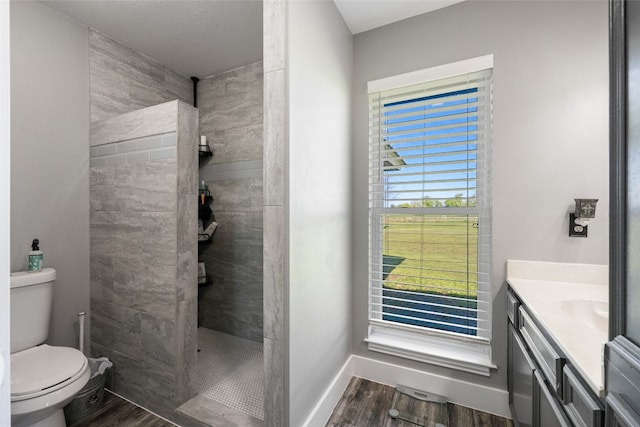 bathroom featuring hardwood / wood-style flooring, vanity, toilet, and tiled shower