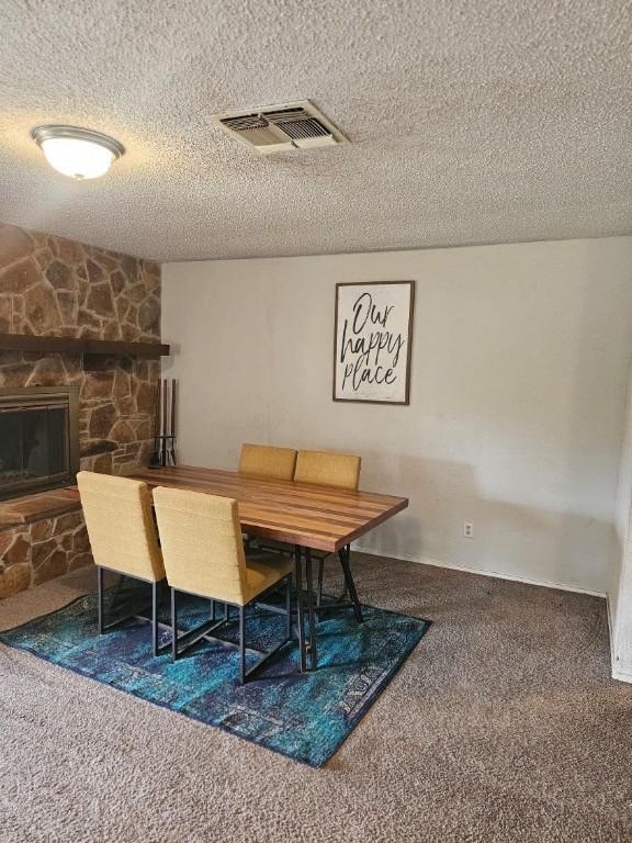 dining room featuring a stone fireplace, carpet floors, and a textured ceiling