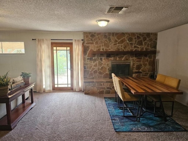 dining space featuring carpet flooring, a stone fireplace, and a textured ceiling