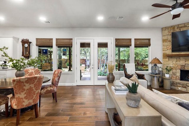 living room featuring ceiling fan, a stone fireplace, dark hardwood / wood-style flooring, and french doors