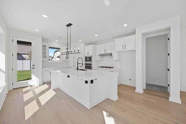 kitchen featuring light wood-type flooring, sink, decorative light fixtures, white cabinetry, and a large island