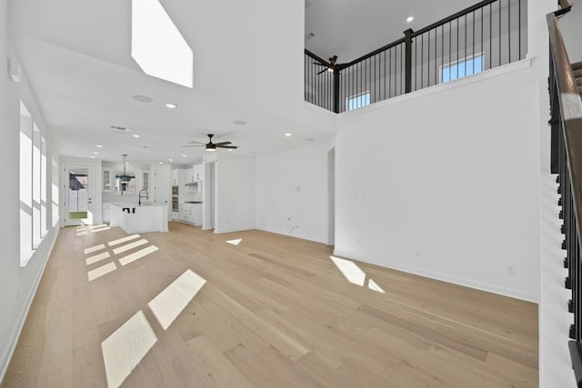 unfurnished living room featuring a high ceiling, light hardwood / wood-style floors, ceiling fan, and sink