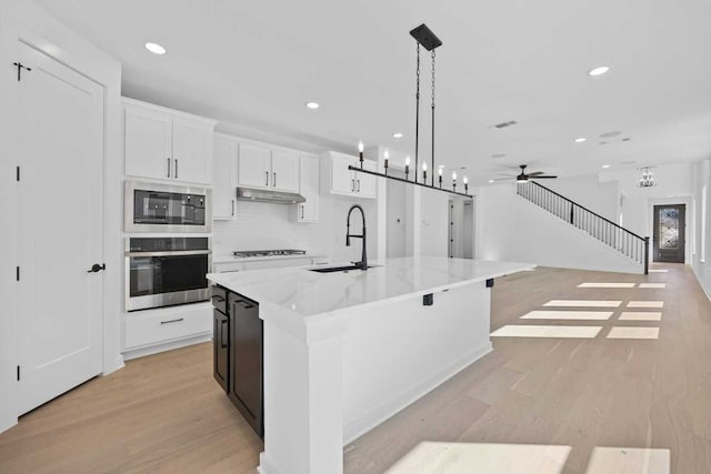 kitchen featuring appliances with stainless steel finishes, a kitchen island with sink, sink, decorative light fixtures, and white cabinets