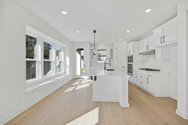 kitchen featuring hanging light fixtures, white cabinetry, a center island with sink, and stainless steel appliances