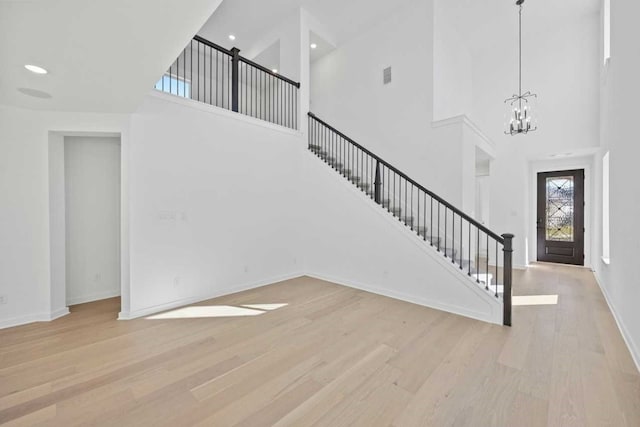 interior space featuring a towering ceiling, a notable chandelier, and light wood-type flooring